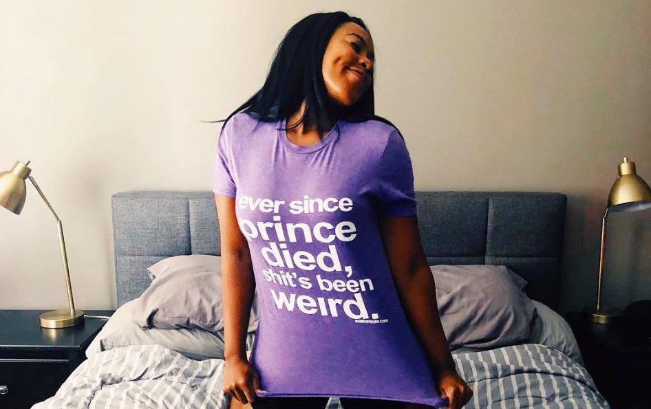 image of a black woman wearing a purple tee shirt reading 'ever since prince died, shit's been weird'. she's smiling and looking to the side.